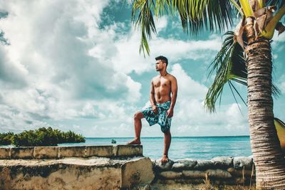 Full length of shirtless man standing at beach against sky