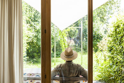 Back view of senior man wearing straw hat on terrace enjoying his garden