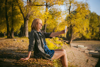 Woman with arms outstretched sitting in park during autumn