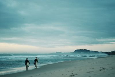 Rear view of surfer walking on shore at beach in queensland