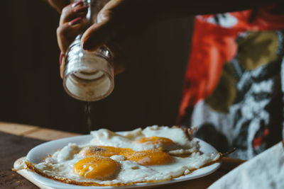 Cropped hands of woman sprinkling pepper on fried eggs at home