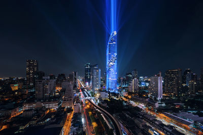 Light trails on road amidst buildings against sky at night