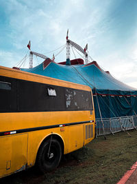 Car bus on field against sky with a circus behind