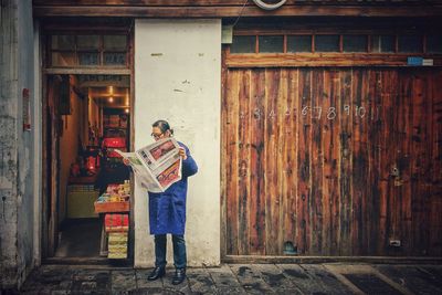 Man reading newspaper outside shop