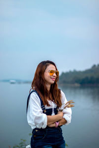 Smiling young woman standing against sky