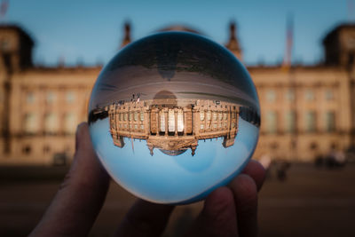 Close-up of hand holding glass of building against sky