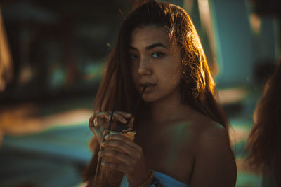 Close-up portrait of young woman drinking drink during sunset