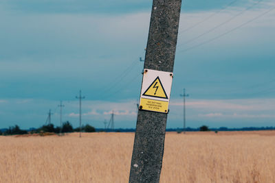 Close-up of sign board on field against sky