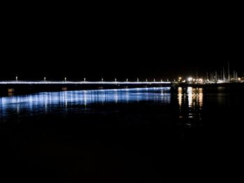 Illuminated bridge over river against sky at night