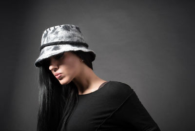 Portrait of young woman wearing hat against black background