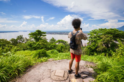 Rear view of woman standing by plants against sky