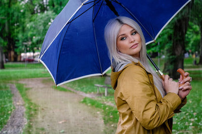 Portrait of happy woman with umbrella standing in rain