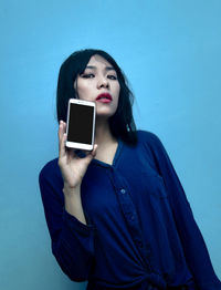 Portrait of young woman using smart phone against blue background