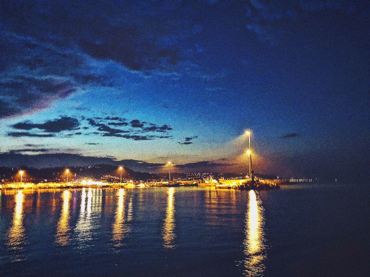 AERIAL VIEW OF ILLUMINATED CITY BY SEA AGAINST SKY