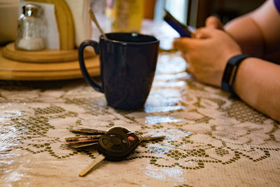Close-up of car key with man in background sitting on table