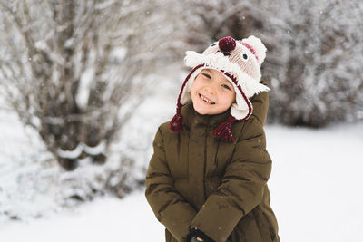 Cute little boy in funny winter hat walks during a snowfall. outdoors winter activities for kids.