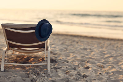 A blue hat hangs on a chaise longue on a beautiful sandy beach by the sea during sunset. 