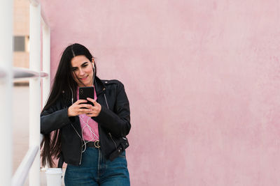 Young woman listen music and looks her smartphone in a pink background