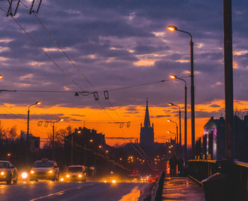 Cars on street against sky at sunset