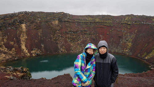 Portrait of couple standing on mountain by lake during winter