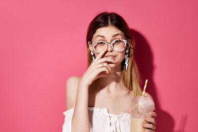 Portrait of woman holding drink against pink background