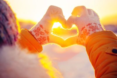 Close-up of hand against orange sky during winter