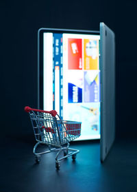 Close-up of shopping cart by digital tablet against black background