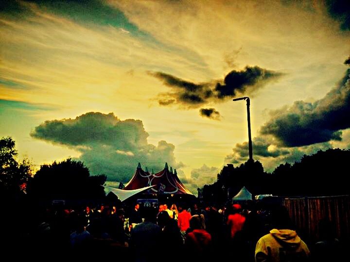 sky, silhouette, cloud - sky, sunset, street light, illuminated, dusk, cloudy, built structure, cloud, lighting equipment, tree, building exterior, night, architecture, outdoors, dramatic sky, large group of people, flag