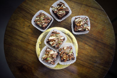 Chocolate brownie cubes with chocolate drizzle in paper cups on a wooden background.