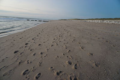 Footprints on sand at beach against clear sky