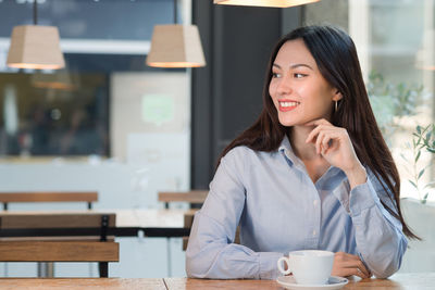 Smiling young woman with coffee cup on table