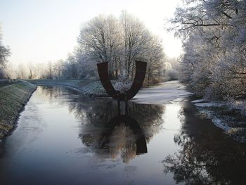 Bare trees by lake against sky during winter