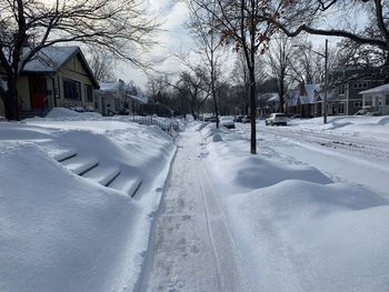 Snow covered road by buildings in city