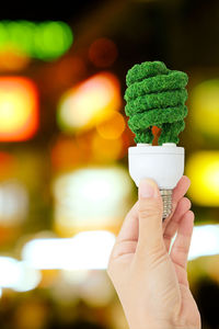 Close-up of hand holding light bulb covered with moss
