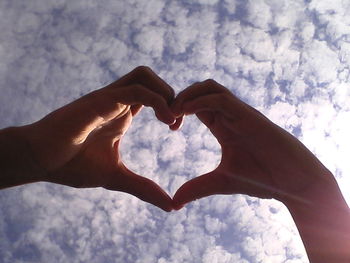 Low angle view of couple making heart shape against cloudy sky