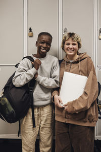 Portrait of happy teenage boy and girl standing against locker in school