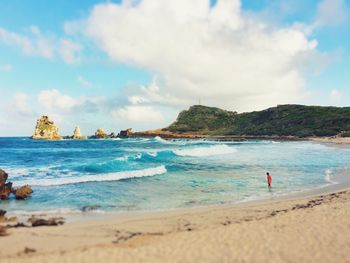 Person walking on beach against cloudy sky