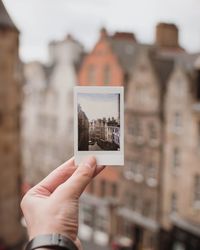 Close-up of person holding photograph against building