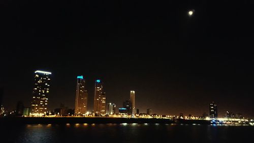 Illuminated city by river against sky at night