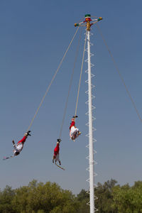 Low angle view of people paragliding against clear sky