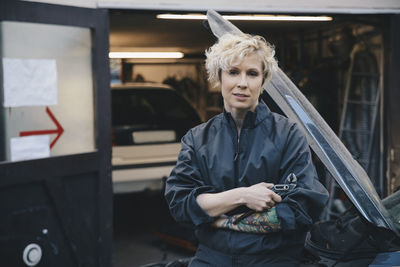 Portrait of confident mechanic leaning on car outside repair shop