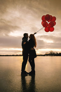 Rear view of woman holding balloons at sunset