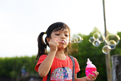 Girl blowing bubbles while standing against sky in park