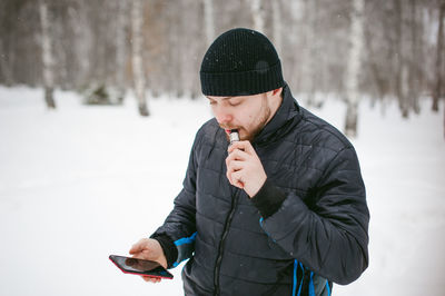 Close-up of man using phone while smoking on snow covered field