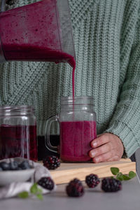 Crop person filling from blender glass jar with yummy vitamin smoothie of sweet fresh berries and mint after preparing breakfast at home