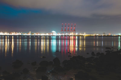 Illuminated city by sea against sky at night