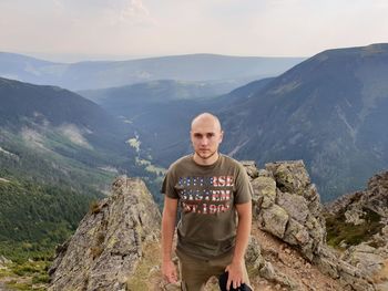 Portrait of young man standing on rock against mountains