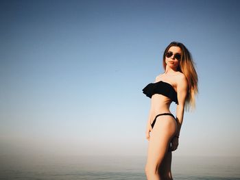 Low angle view of beautiful woman in bikini standing against sea on sunny day