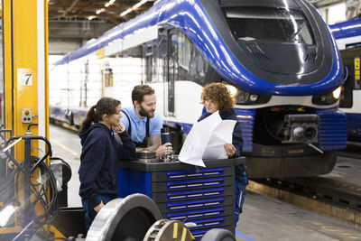 Trainees discussing with engineer over blueprint at factory