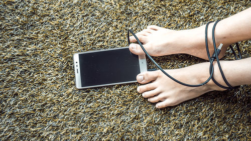 Low section of woman leg tied with mobile phone cable on rug